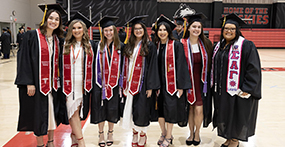 Members of NIU Sororities pose for photo while wearing caps, gowns and Greek stolls at commencement