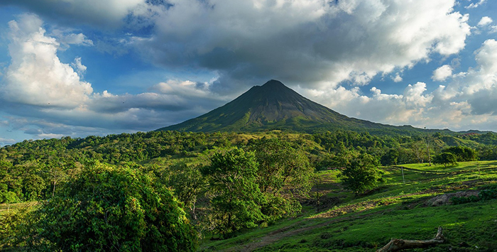 A volcano in Costa Rica surrounded by a lush green valley and clouds in a clear blue sky.