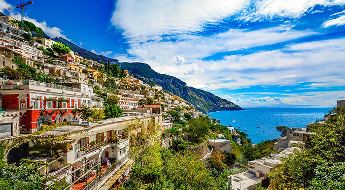 Scenic view of the Amalfi Coast with colorful buildings terraced on steep hills overlooking the Mediterranean Sea under a partly cloudy sky.