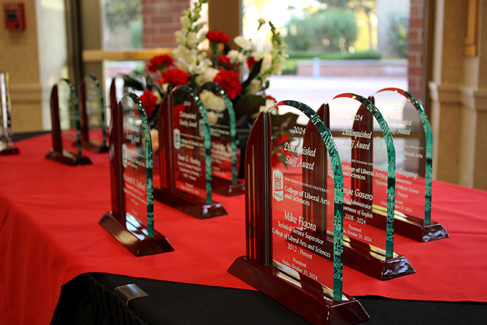 Photo of a table with red and black table cloths where several Distinguished Award plaques are displayed. There are red and white flowers in a center piece also on the table.
