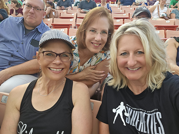 Huskie Marching Band Alumni Network members pose for photo in the stands at Huskie Stadium during the summer social event.