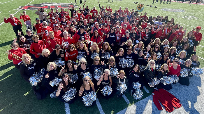 Alumni members of the Huskie Marching Band and Silverettes pose on the field at Huskie Stadium after a Homecoming game