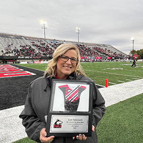 Lori Valenzuela holding a plaque presented to her on the sidelines of an NIU football game.