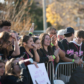 A large crowd stands behind a fence watching the Women's Tugs competition at NIU