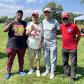 Four male Black NIU alumni pose for a photo making the Huskie hand sign at the BAC reunion picnic.