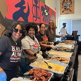 Four female Black NIU alumni serve a meal during the BAC 2025 Homecoming events.