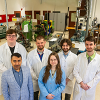 Six NIU Bioplastics Lab students and professors pose in a lab while wearing lab coats
