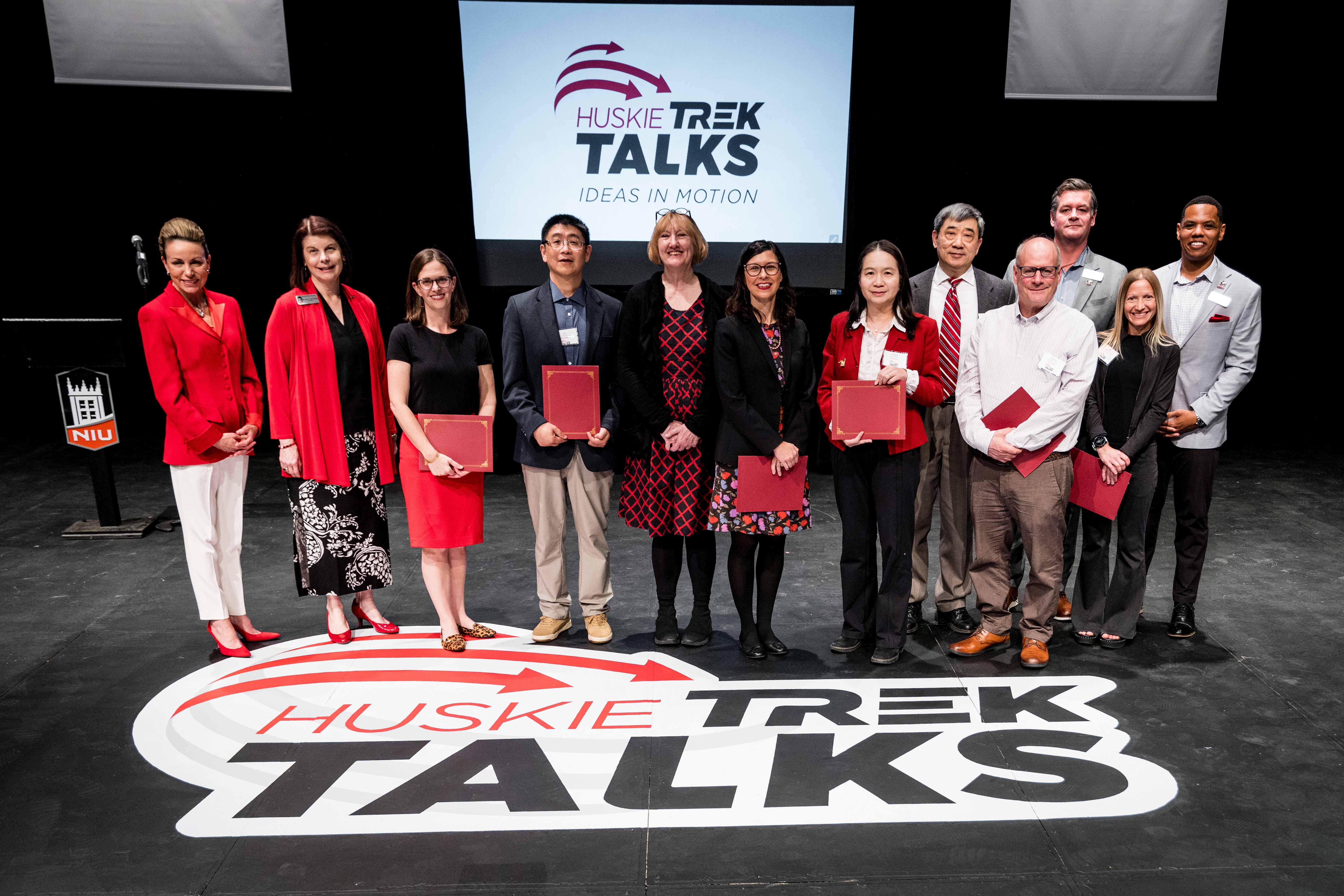 Huskie Trek Talks 2026 Participants join NIU leadership and Stacey Barsema (left), NIU Foundation Board of Directors grants committee chairperson, on stage on April 18.