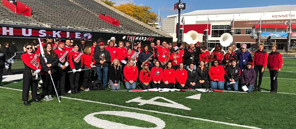 Members of the Huskie Marching Band Alumni Network pose for a photo on the football field at Huskie Stadium